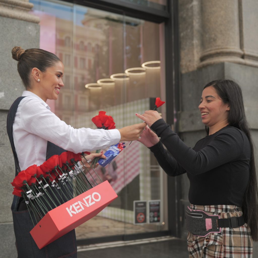Mujeres intercambiando flores rojas en acción promocional de Kenzo