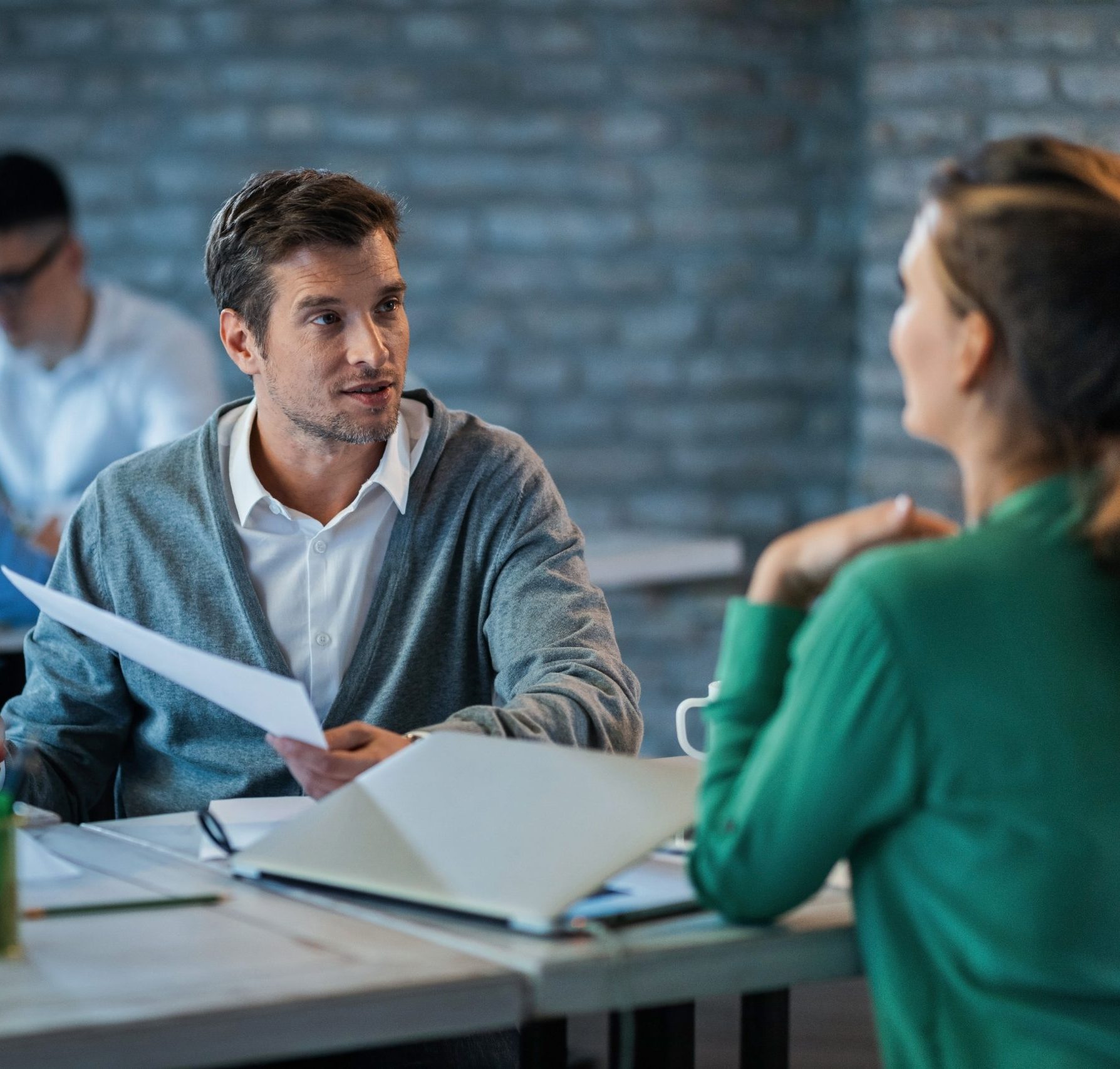 male entrepreneur discussing about business reports with female colleague while working office desk there are people background scaled e1787573052882